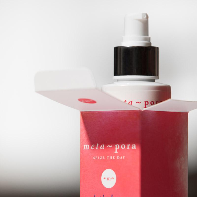 Red bottle with black cap and 'meta~pora' branding on a white background