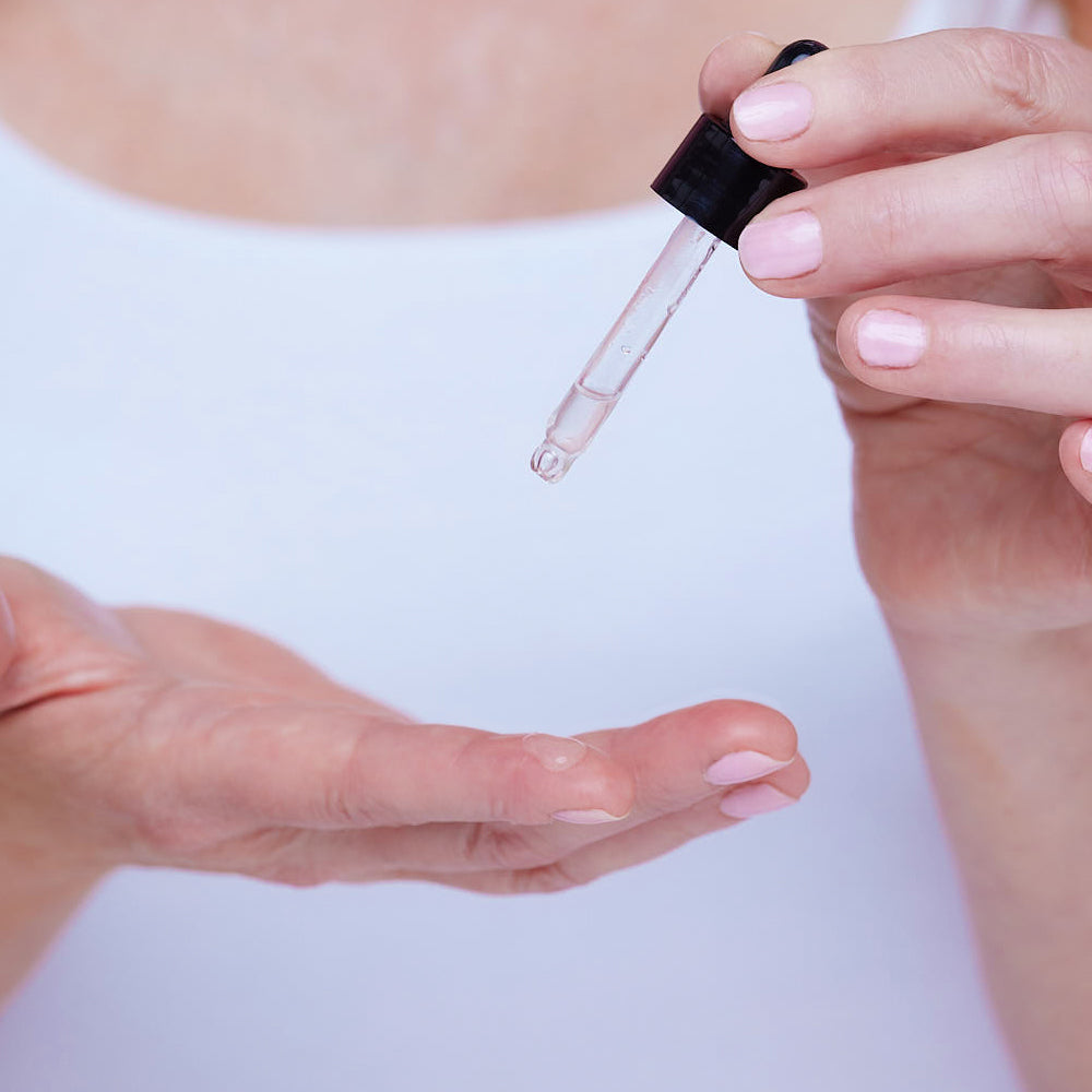 Person holding a dropper with clear liquid against a white background