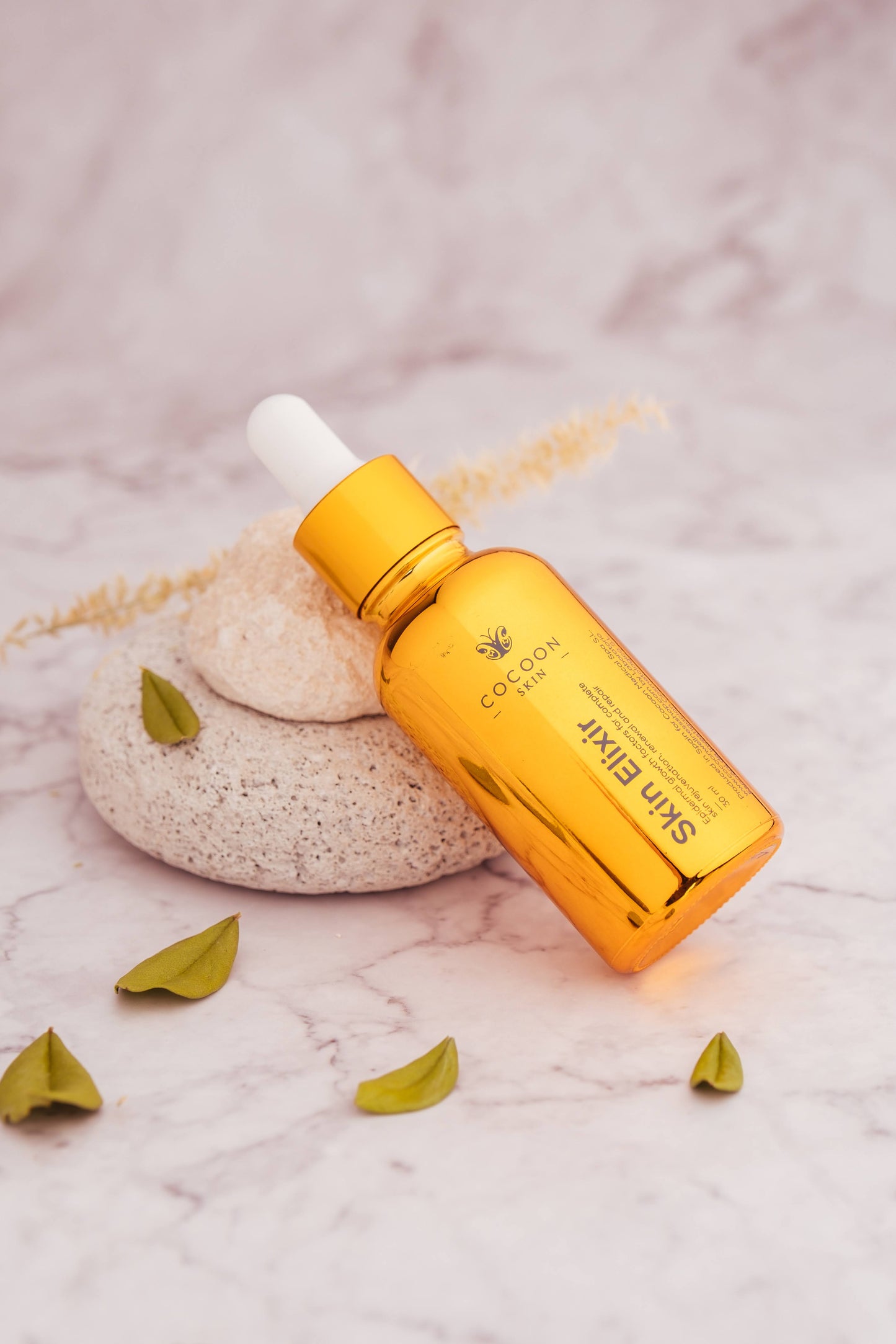 Orange bottle of 'Sun Elixir' with dropper on a textured surface with green leaves.