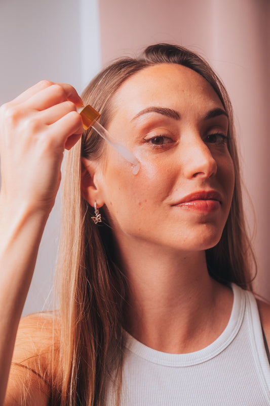 Woman applying a dropper of skincare product to her face.