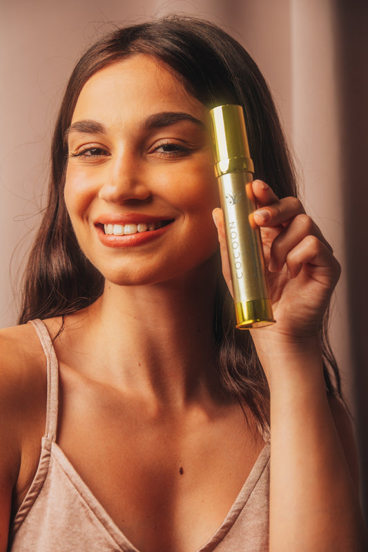Woman holding a gold cosmetic bottle against a neutral background